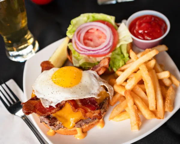 Bacon cheeseburger topped with a fried egg, served with fries, lettuce, tomato, and ketchup